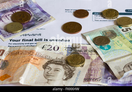 An overdue utility bill, partially covered with a variety of sterling banknotes and coins. Stock Photo