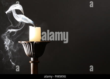 Extinguished candle in candlestick with smoke on dark background Stock Photo