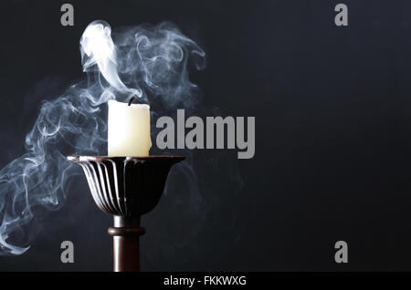Extinguished candle in candlestick with smoke on dark background Stock Photo