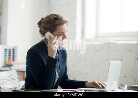 Portrait of beautiful happy smiling young designer woman working on laptop at office desk. Attractive cheerful model in suit