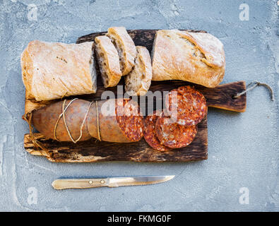Wine snack set. Hungarian mangalica pork salami sausage and rustic bread on dark wooden board over a rough grey-blue concrete ba Stock Photo