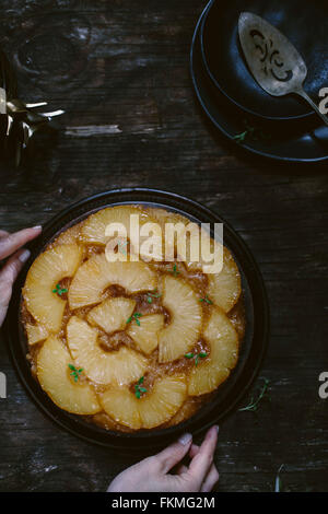 A woman is placing an upside down pineapple cake on a reclaimed wood table. Stock Photo