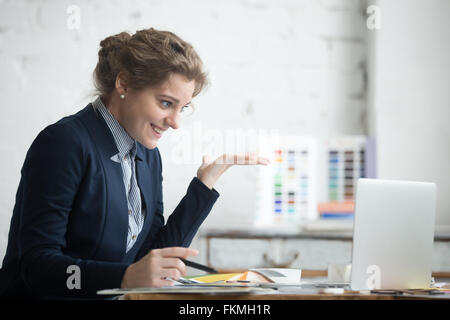 Portrait of young smiling shocked business woman wearing suit sitting at home office desk using laptop, looking at computer Stock Photo