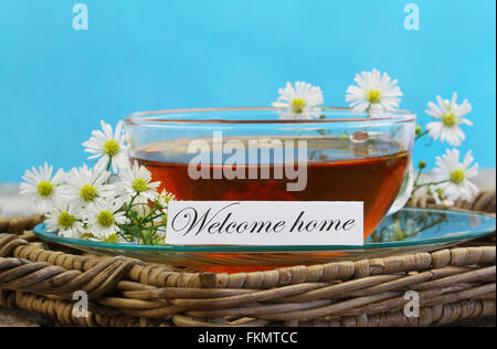 Welcome home card with cup of chamomile tea with fresh chamomile flowers on wicker tray Stock Photo