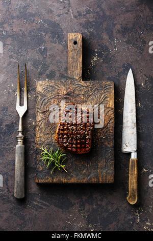 Grilled marbled meat Steak with rosemary and meat fork and kitchen knife on cutting board on dark background Stock Photo