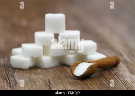 White sugar on wooden scoop and white sugar cubes stacked up in the background Stock Photo