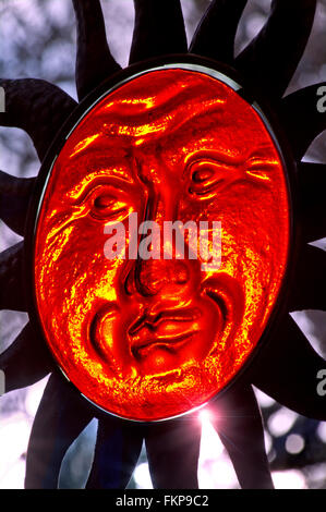 Translucent glass face of Sun God sculpture and extending rays with low setting sun illuminating its features Stock Photo