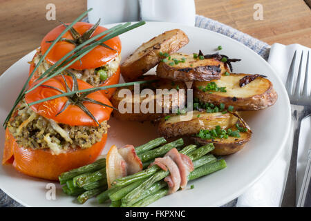 A meal of Fresh oven baked Beef Tomatoes stuffed with a Duxelle of Mushroom, Onion Saffron rice and Cheese with potatoes and veg Stock Photo