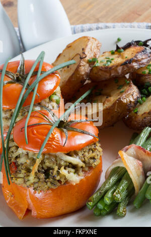 A meal of Fresh oven baked Beef Tomatoes stuffed with a Duxelle of Mushroom, Onion Saffron rice and Cheese with potatoes and veg Stock Photo