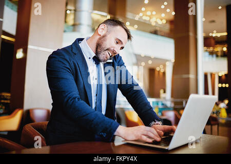 Smiling businessman talking on the phone and typing on laptop Stock Photo
