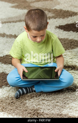 Boy using a tablet sitting on the floor Stock Photo