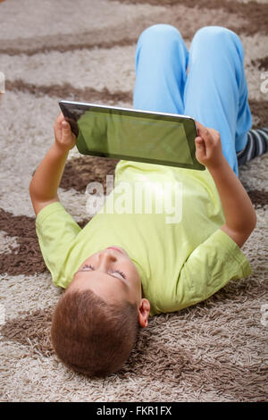 Child holding digital tablet, lying on a carpet Stock Photo