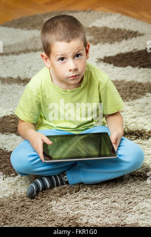 Boy using a tablet sitting on the floor Stock Photo