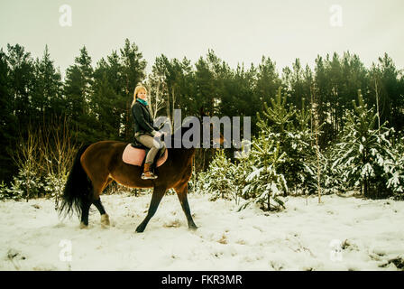Caucasian woman riding horse on snowy path Stock Photo