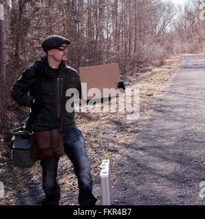 Man hitchhiking with blank sign on rural road Stock Photo