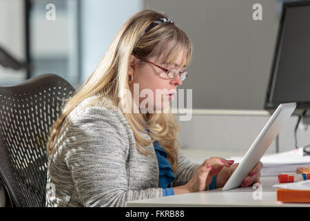 Caucasian businesswoman with Down Syndrome using digital tablet in office Stock Photo