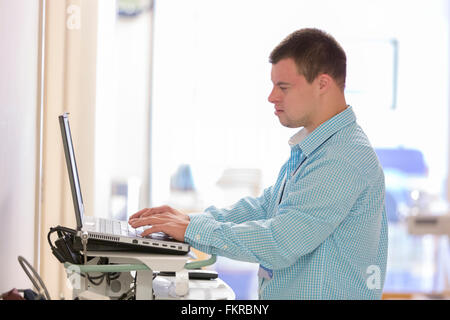 Caucasian man with Down Syndrome working on laptop in hospital Stock Photo