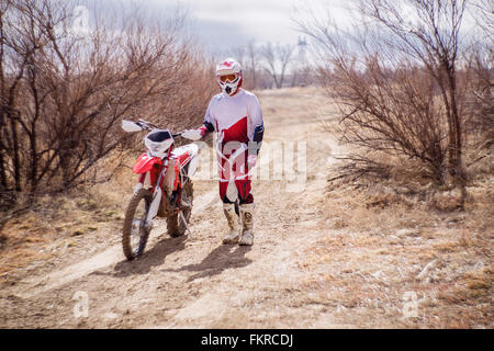 Dirt bike rider standing with motorcycle in rural field Stock Photo