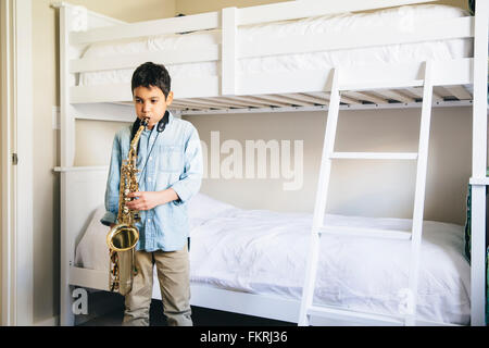 Mixed race boy playing saxophone in bedroom Stock Photo
