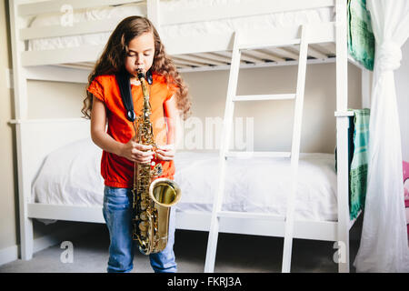 Mixed race girl playing saxophone in bedroom Stock Photo