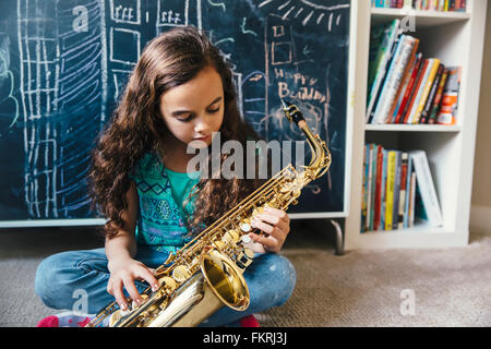 Mixed race girl playing saxophone on floor Stock Photo