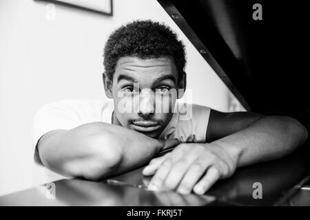 Mixed race man leaning on piano Stock Photo
