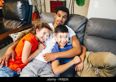 Mixed race brothers and sister laying on sofa Stock Photo