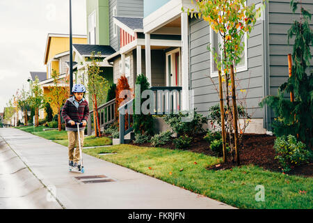 Mixed race boy riding scooter on sidewalk Stock Photo