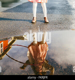 Mixed race girl and plastic hoop reflected in puddle Stock Photo