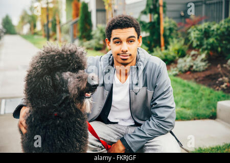 Mixed race man petting dog on sidewalk Stock Photo
