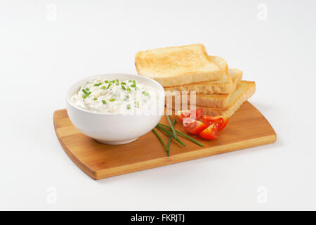 stack of fresh toasts and bowl of chives spread on wooden cutting board Stock Photo