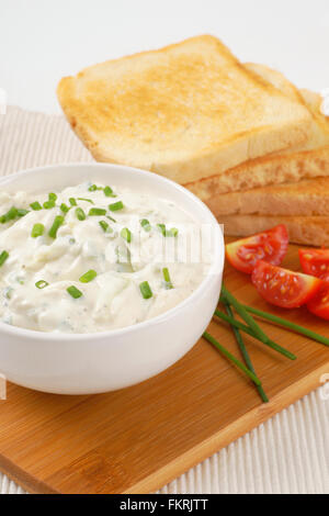 stack of fresh toasts and bowl of chives spread on wooden cutting board Stock Photo