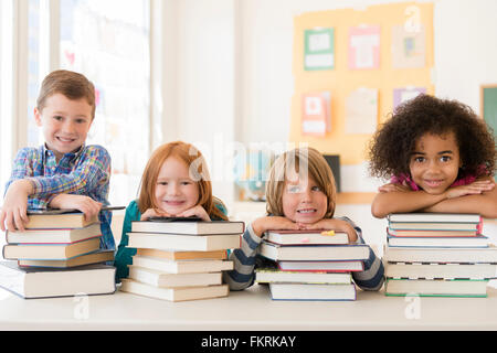 Students resting on stacks of books in classroom Stock Photo