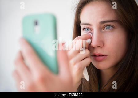 Native American woman with cell phone wiping away tears Stock Photo