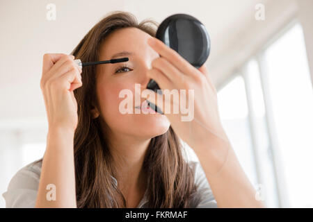 Mixed race woman applying makeup in compact mirror Stock Photo