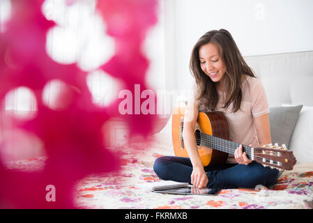 Mixed race woman playing guitar on bed Stock Photo