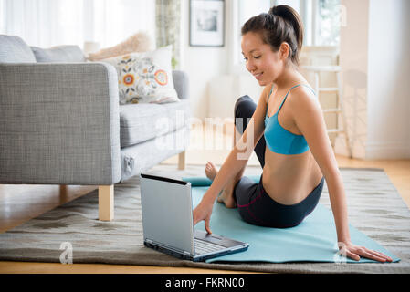 Mixed race woman doing yoga video in living room Stock Photo