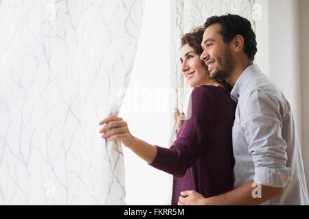 Couple looking out window curtain Stock Photo