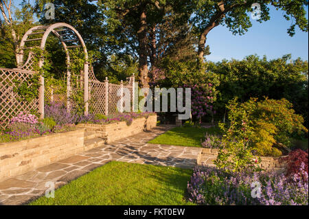 Sunlit path, flowering plants, wall, steps, trellis arch & screen - beautiful, traditional, designed, landscaped, garden, West Yorkshire, England, UK. Stock Photo