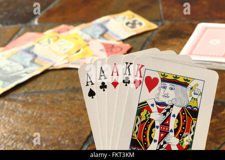 A 'Full House'  hand of cards in the foreground with Australian banknotes laying on a tiled table top Stock Photo
