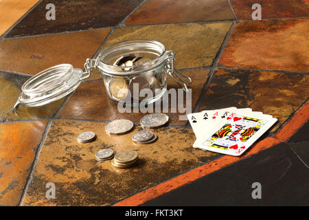 A small jar containing Australian coins with coins and playing cards showing a 'full house' on a tiled table top. Stock Photo
