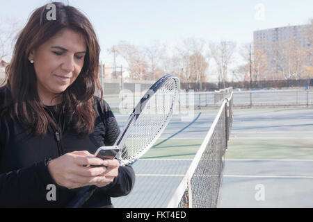 Hispanic woman using cell phone on tennis court Stock Photo