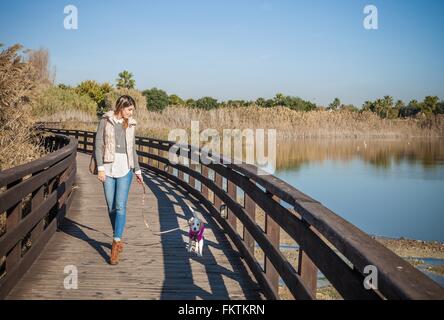 Full length front view   young woman wooden elevated walkway walking dog Stock Photo