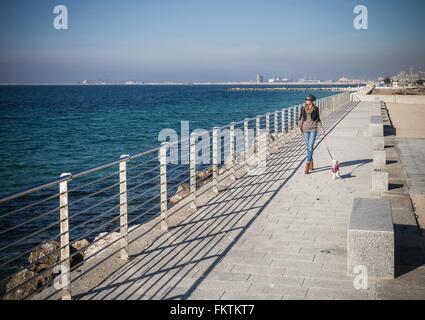 Full length front view young woman walking dog on seafront looking away Stock Photo