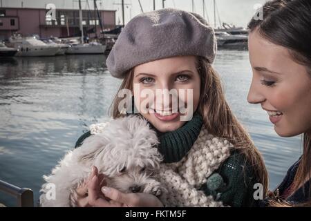 Young woman wearing beret in boatyard holding dog looking at camera smiling Stock Photo