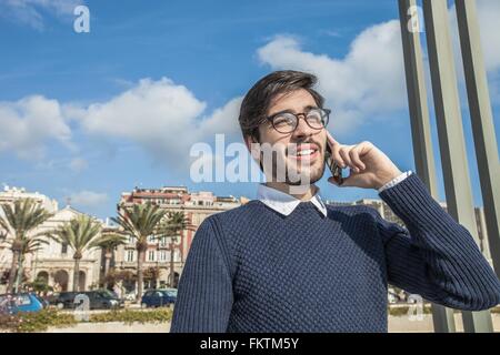 Young man wearing eyeglasses using smartphone looking away smiling Stock Photo