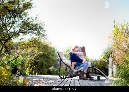 Mother and daughter hugging on lounge chair on decking Stock Photo