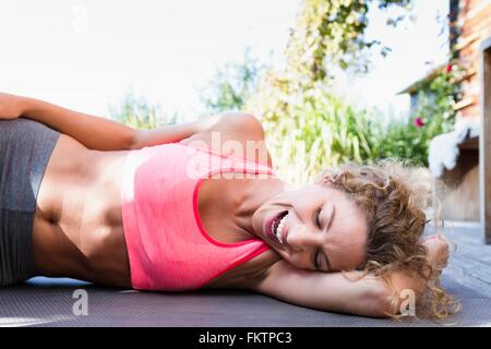 Young woman resting on yoga mat in pink crop top, laughing Stock Photo