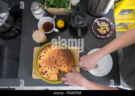 Overhead view of female hand slicing baked cake at kitchen counter Stock Photo