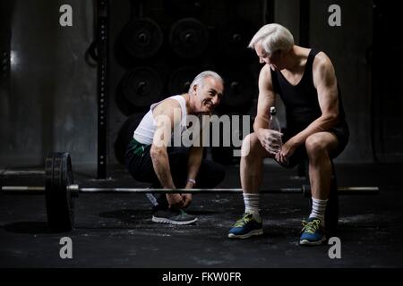 Senior men chatting and tying trainer laces in dark gym